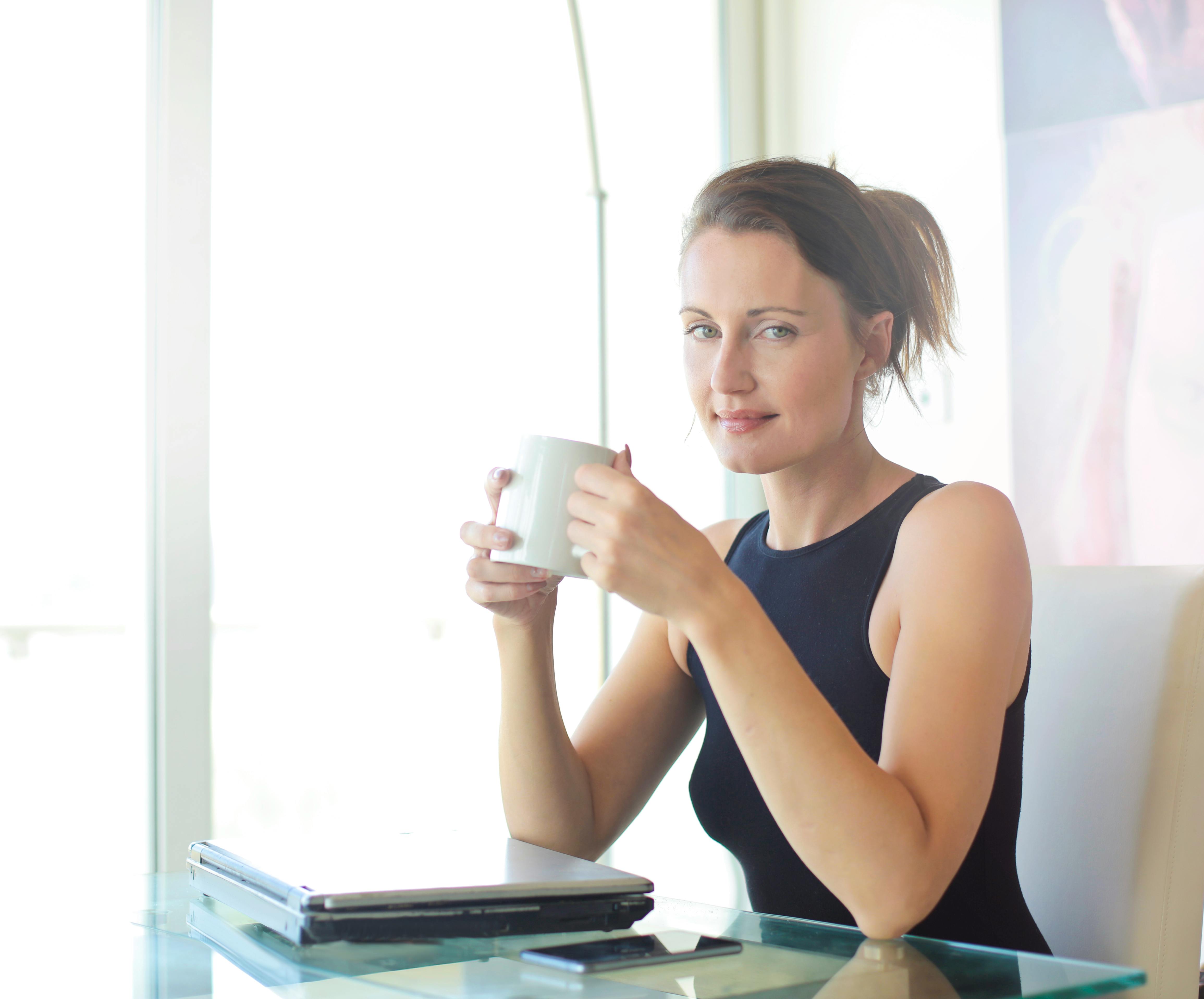 Young woman sitting at her desk, holding a coffee cup and smiling. Ideal for workplace and lifestyle themes.